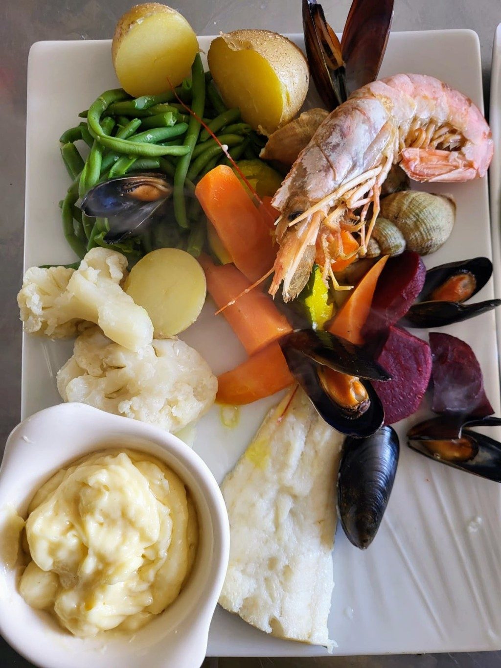 Une assiette de fruits de mer et de légumes vapeur, avec un ramequin de sauce